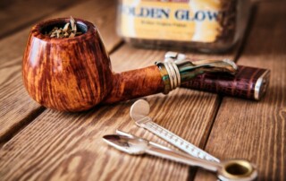 A wooden smoking pipe filled with tobacco, beside merchant services tools and a tin labeled "golden glow," on a wooden surface.